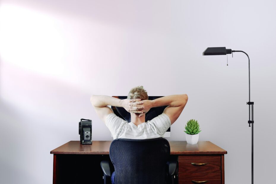 A man touching his head seated in front of his desk.